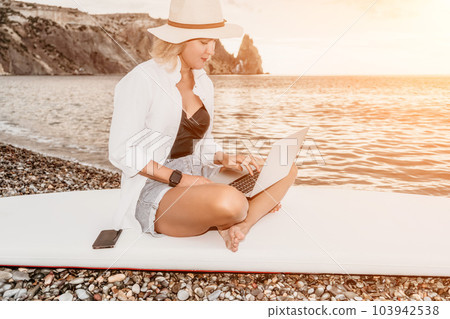 Digital nomad, Business woman working on laptop by the sea. Pretty lady typing on computer by the sea at sunset, makes a business transaction online from a distance. Freelance, remote work on vacation 103942538