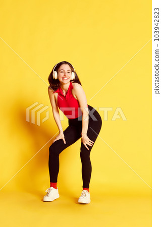 Full-length portrait of young beautiful woman in casual clothes listening to music in headphones and dancing against yellow studio background 103942823