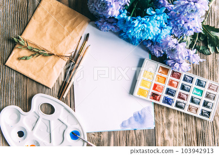 Palette of watercolor paints, brushes and paper for a water color on wooden background, close up. Flat lay, spring background with copy space Palette of watercolor paints, brushes and paper for a water color on wooden background, close up. Flat lay, spring background with copy space 103942913