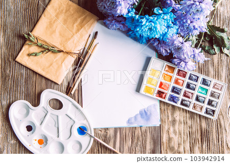 Palette of watercolor paints, brushes and paper for a water color on wooden background, close up. Flat lay, spring background with copy space Palette of watercolor paints, brushes and paper for a water color on wooden background, close up. Flat lay, spring background with copy space 103942914