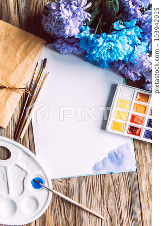 Palette of watercolor paints, brushes and paper for a water color on wooden background, close up. Flat lay, spring background with copy space 103942915
