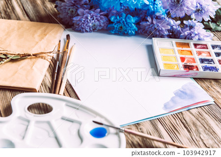 Palette of watercolor paints, brushes and paper for a water color on wooden background, close up. Flat lay, spring background with copy space Palette of watercolor paints, brushes and paper for a water color on wooden background, close up. Flat lay, spring background with copy space 103942917
