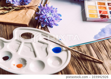 Palette of watercolor paints, brushes and paper for a water color on wooden background, close up. Flat lay, spring background with copy space 103942926