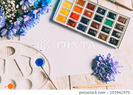 Palette of watercolor paints, brushes and paper for a water color on wooden background, close up. Flat lay, spring background with copy space Palette of watercolor paints, brushes and paper for a water color on wooden background, close up. Flat lay, spring background with copy space 103942970