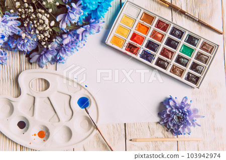 Palette of watercolor paints, brushes and paper for a water color on wooden background, close up. Flat lay, spring background with copy space 103942974