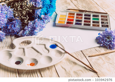 Palette of watercolor paints, brushes and paper for a water color on wooden background, close up. Flat lay, spring background with copy space Palette of watercolor paints, brushes and paper for a water color on wooden background, close up. Flat lay, spring background with copy space 103942976