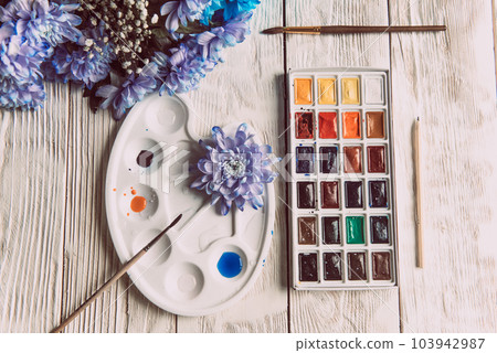 Palette of watercolor paints, brushes and paper for a water color on wooden background, close up. Flat lay, spring background with copy space Palette of watercolor paints, brushes and paper for a water color on wooden background, close up. Flat lay, spring background with copy space 103942987