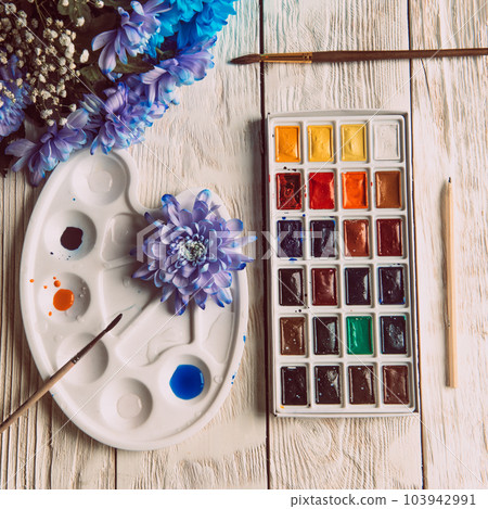 Palette of watercolor paints, brushes and paper for a water color on wooden background, close up. Flat lay, spring background with copy space Palette of watercolor paints, brushes and paper for a water color on wooden background, close up. Flat lay, spring background with copy space 103942991