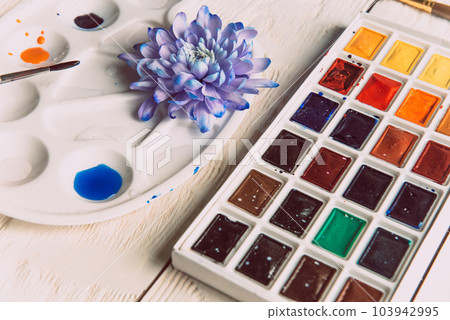 Palette of watercolor paints, brushes and paper for a water color on wooden background, close up. Flat lay, spring background with copy space 103942995