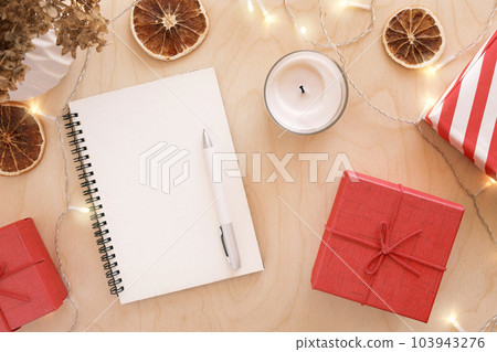 Christmas wish list writing. Woman creating present list for winter holidays. Top view, flat lay. Preparing for Xmas and New Year concept. Female hand writing in empty notebook on wooden table 103943276