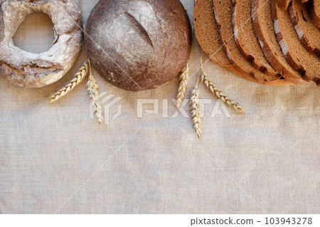 Baked bread. Loaf of Bread. Fresh Bakery Products on Wooden Board. Healthy Food Concept. Top View. Flat lay. Slices of Homemade Sourdough Bread with Flour on Rustic Linen Background. Wheat Spikes 103943278