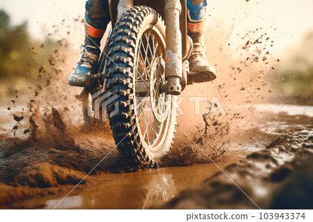 Close-up shot of the front wheel of a motocross bike riding along a muddy dirt track - Generative AI 103943374