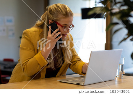 Plus size caucasian casual businesswoman in glasses using laptop and talking on phone at desk Plus size caucasian casual businesswoman in glasses using laptop and talking on phone at desk 103943901