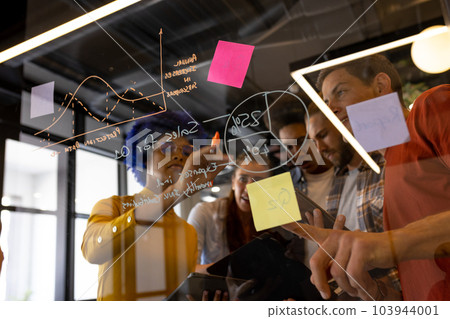 Diverse creative colleagues in discussion brainstorming making notes on glass wall in office 103944001