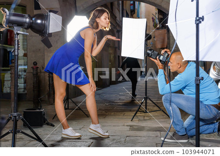 Professional photo shooting outdoors. Attractive female model posing to photographer on city street Professional photo shooting outdoors. Attractive female model posing to photographer on city street 103944071