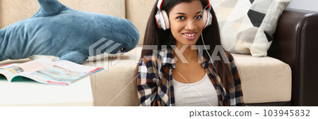 Young beautiful african american woman relaxing and listening to music with headphones on floor Young beautiful african american woman relaxing and listening to music with headphones on floor 103945832