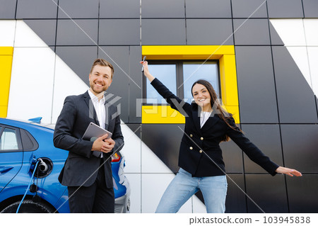 Happy female client standing at brand new car and taking keys from dealer in dealership outdoor. The woman is very happy with the new car, holding the keys in her hands Happy female client standing at brand new car and taking keys from dealer in dealership outdoor. The woman is very happy with the new car, holding the keys in her hands 103945838