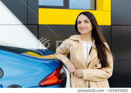 Woman is standing at the car and charging electric car at the charging station 103945902