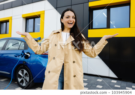 Woman is standing at the car and charging electric car at the charging station 103945904