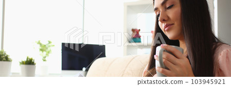 Young woman is reading book and holding cup in living room on sofa 103945921
