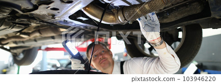 Mechanic with a lamp inspects suspension of car on lift Mechanic with a lamp inspects suspension of car on lift 103946220