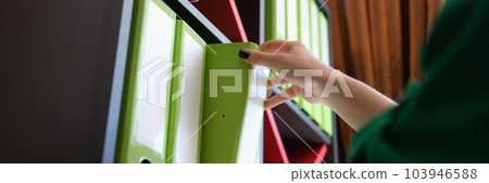 Female hands takes folder with documents from shelf in archive 103946588