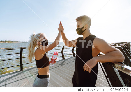 Young man and woman in protective masks running and doing exercises outdoors in the morning. Sport, Active. 103946904