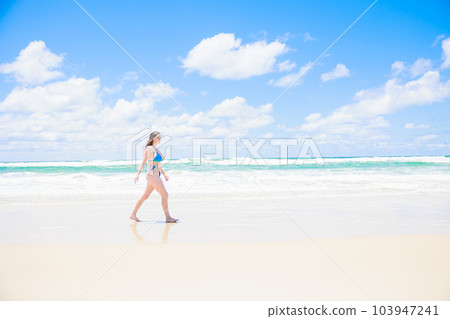 Caucasian woman in bikini walking in front of blue sky and sea 103947241