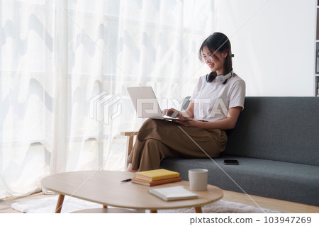 Young relaxed smiling pretty woman relaxing sitting on sofa at home. Female feeling joy enjoying with laptop on cozy couch 103947269