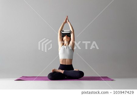 Young girl with slim body, wearing VR glasses and training in sportswear against grey studio background. Yoga and meditation session 103947429