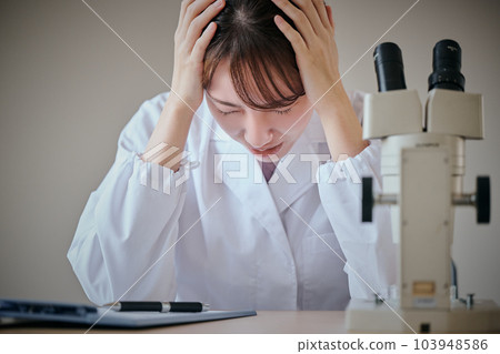 A young woman in a white coat who is worried about holding her head A young woman in a white coat who is worried about holding her head 103948586