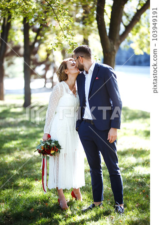 Couple enjoying romantic moments in park. Elegant bride in beautiful white dress, groom in a suit. 103949191