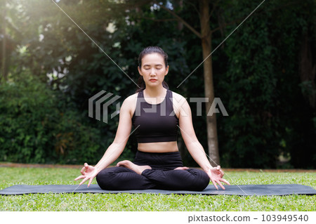 Asian woman practicing yoga in Root Bond, Mula Bandha pose on the mat in outdoor park. 103949540