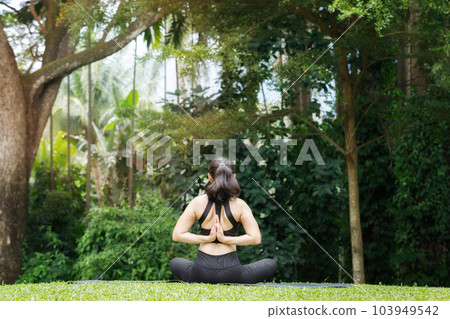 Asian woman practicing yoga in reverse prayer lotus pose, back and shoulders stretching in outdoor park. 103949542