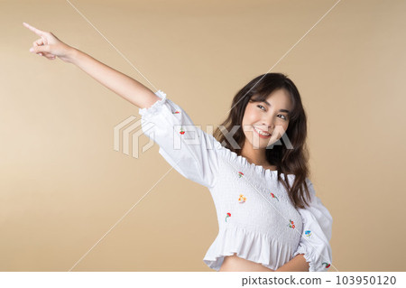 Young smiling Asian woman pointing finger sideways to copy space in brown color background. Young smiling Asian woman pointing finger sideways to copy space in brown color background. 103950120