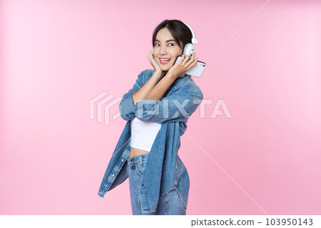 Young Asian woman wearing headphones dancing and listening to music from smartphone shoot in isolated on pink background 103950143