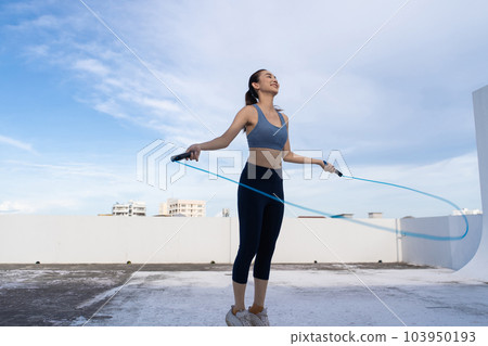 Young Asian woman with jump rope on rooftop. Fitness female doing skipping workout outdoors Young Asian woman with jump rope on rooftop. Fitness female doing skipping workout outdoors 103950193
