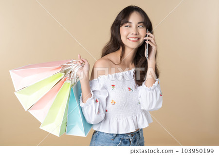Young Asian woman usin shopping bag using phone on isolate brown background 103950199