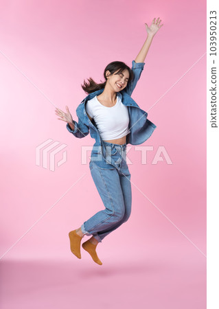 Young Asian woman raises her arm and jumping in a studio shot, expressing happiness and success isolated pink background 103950213