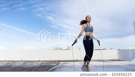 Young Asian woman with jump rope on rooftop. Fitness female doing skipping workout outdoors Young Asian woman with jump rope on rooftop. Fitness female doing skipping workout outdoors 103950225