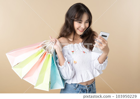 Young Asian woman carrying colorful bags shopping online with mobile phone isolate brown background. Young Asian woman carrying colorful bags shopping online with mobile phone isolate brown background. 103950229