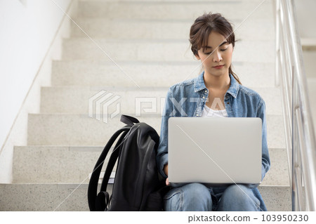 Asian student woman working on a laptop on stairs on university campus. Asian student woman working on a laptop on stairs on university campus. 103950230
