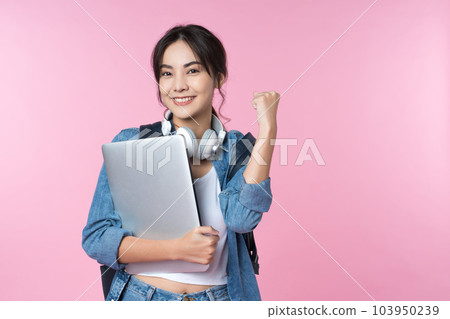 Portrait of smiling young Asian college student with laptop and backpack isolated over pink background.Cheer up success celebration concept Portrait of smiling young Asian college student with laptop and backpack isolated over pink background.Cheer up success celebration concept 103950239