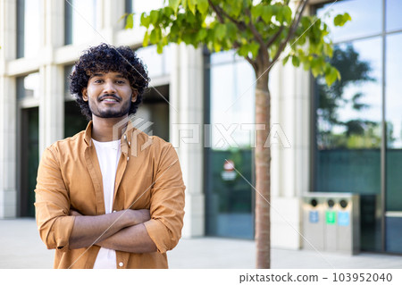 Portrait of young hispanic freelancer businessman outside office building, successful man looking at camera and smiling and with wrinkled hands, worker with curly hair and wearing a shirt. Portrait of young hispanic freelancer businessman outside office building, successful man looking at camera and smiling and with wrinkled hands, worker with curly hair and wearing a shirt. 103952040