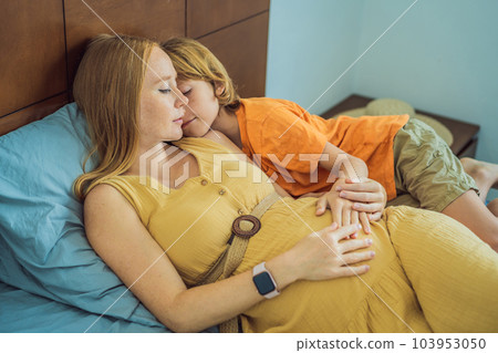 Young pregnant mother hugging her little boy lying in bed at night. Caring and loving parent hugging child Young pregnant mother hugging her little boy lying in bed at night. Caring and loving parent hugging child 103953050