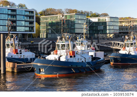Many modern powerful tow ships service team mored in row at Hamburg Elbe harbour at evening sunset day time. Support tugboat vessel fleet in Germany industrial cargo freight harbor marine Many modern powerful tow ships service team mored in row at Hamburg Elbe harbour at evening sunset day time. Support tugboat vessel fleet in Germany industrial cargo freight harbor marine 103953074