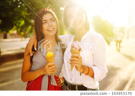 Two young female friends having fun and eating ice cream. Young women enjoy summer and vacation. Two young female friends having fun and eating ice cream. Young women enjoy summer and vacation. 103953170