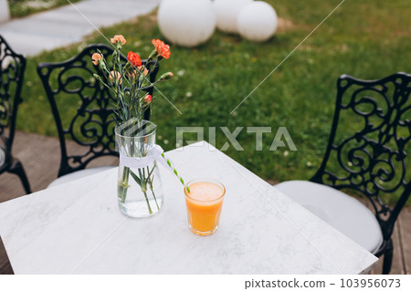 Full glass of orange juice close-up. Fresh orange juice on marble table on the cafe terrace on the street. Glass of yellow lemonade in a summer cafe. Selective focus. Full glass of orange juice close-up. Fresh orange juice on marble table on the cafe terrace on the street. Glass of yellow lemonade in a summer cafe. Selective focus. 103956073