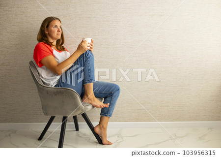 Young beautiful woman in casual wear sitting in armchair with cup of hot coffee 103956315
