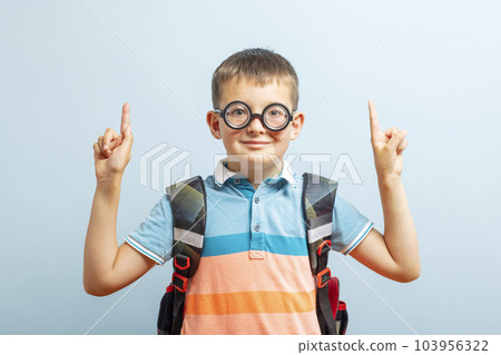 Happy school boy pointing fingers up showing something on blue background Happy school boy pointing fingers up showing something on blue background 103956322